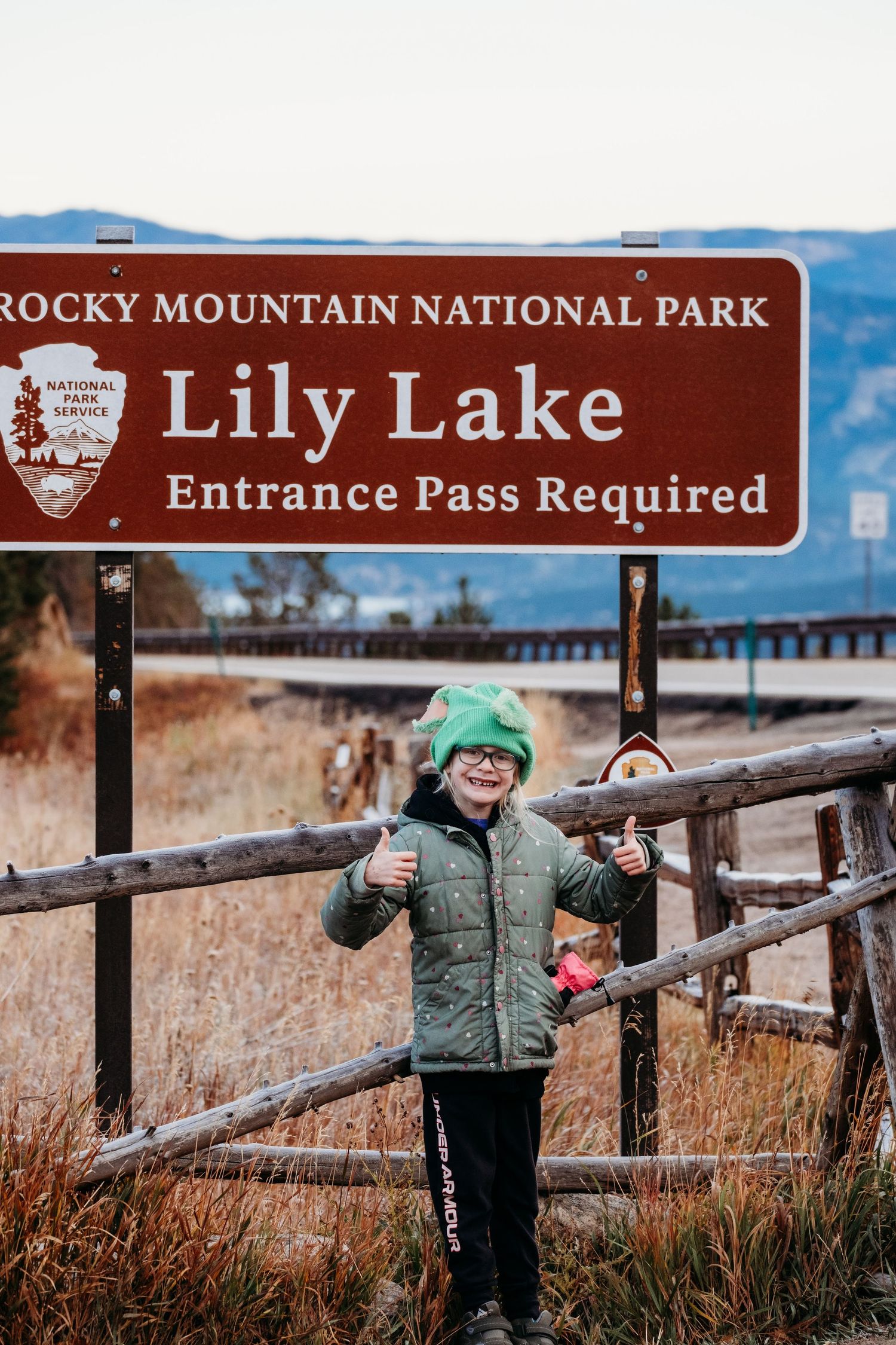 Young girl standing in front of Rocky Mountain National Park Lily Lake's sign.