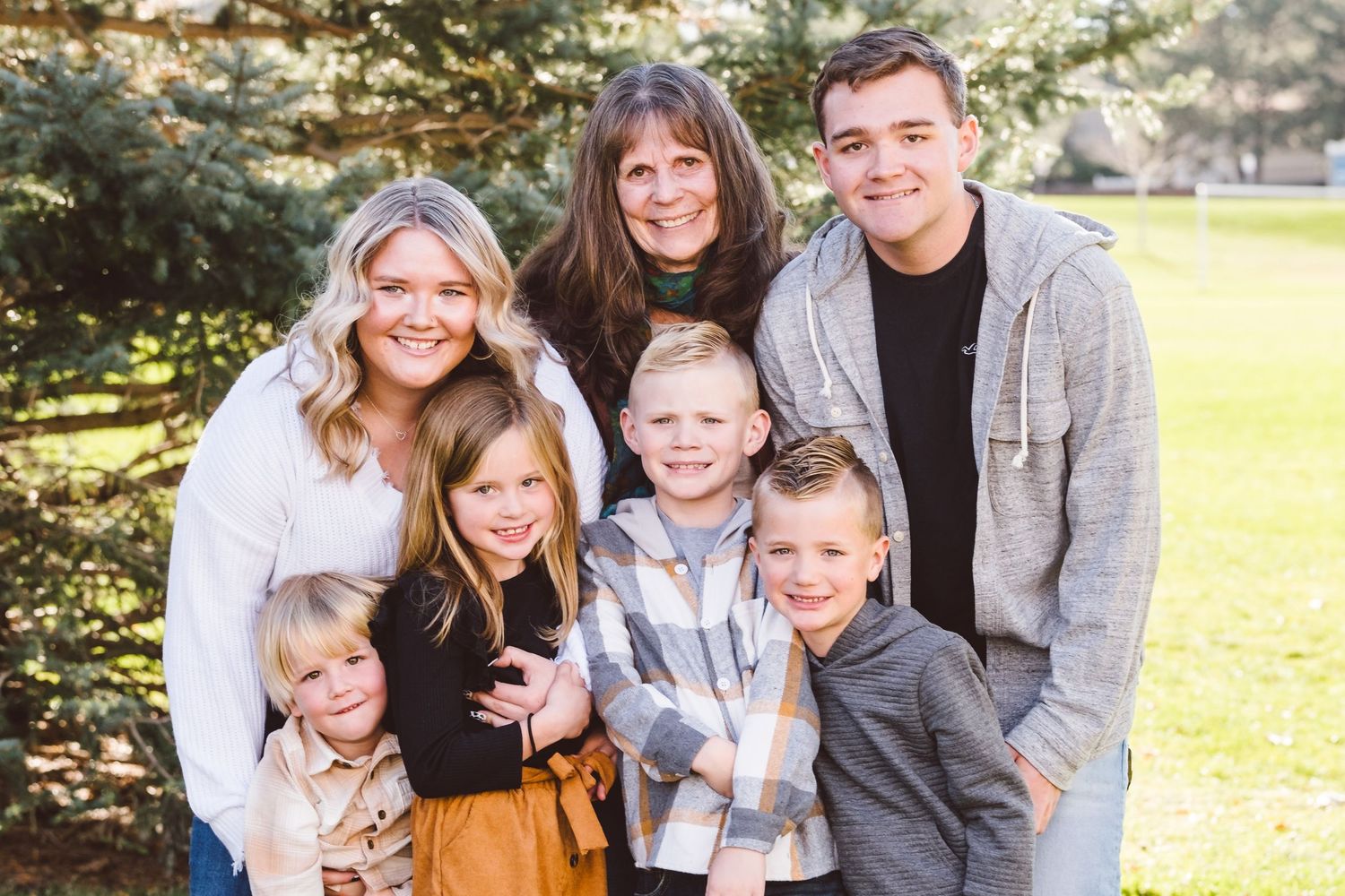 Portrait of grandmother standing with two young adult grandchildren and four young grandchildren, all snuggled close, smiling.