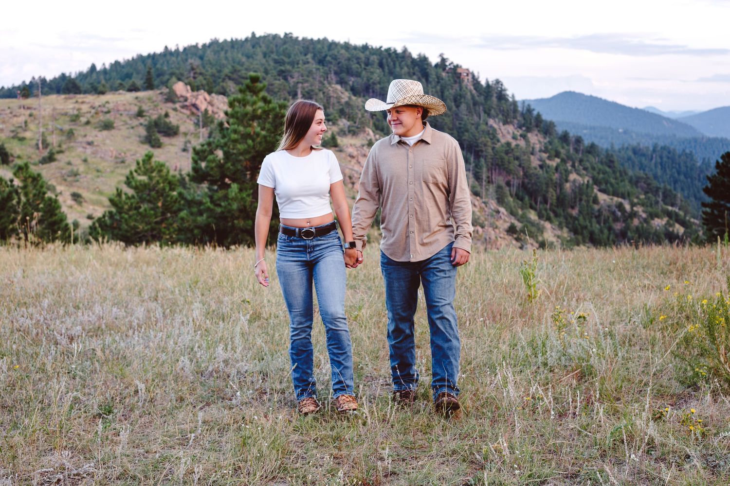 Young couple walking together in field at Mount Falcon West, foothills in background, both looking and smiling at each other.