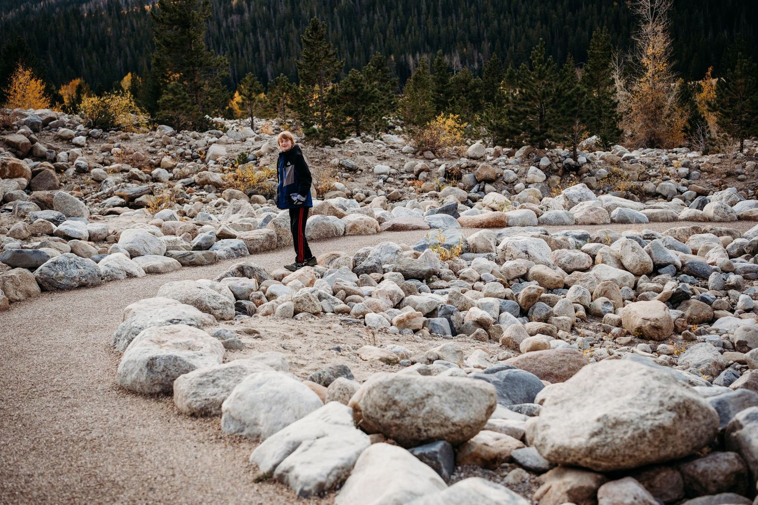 Boy playing on rocks near dirt path at Alluvial Fan in Rocky Mountain National Park.