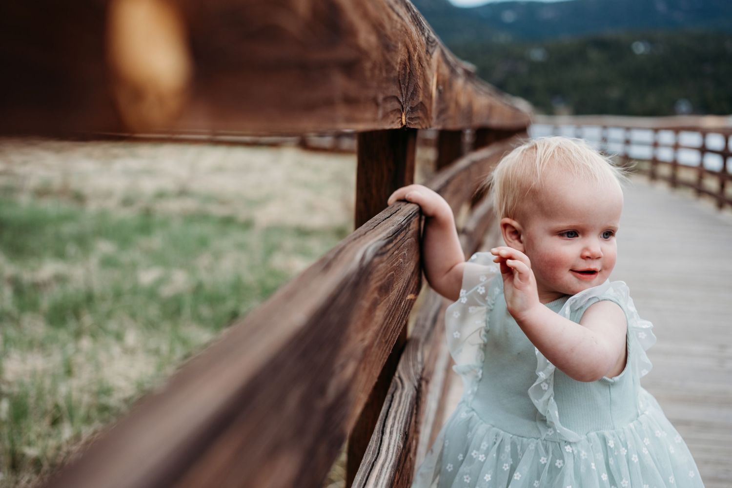 Toddler girl holding onto wooden railing on boardwalk at Evergreen Lake House.