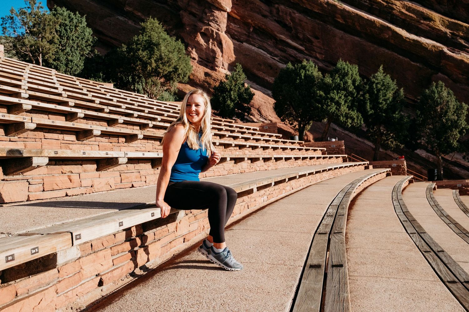 Progress with Paige branding photography session at Red Rocks Amphitheatre, sitting on Red Rocks steps, trees and Red Rocks in background.