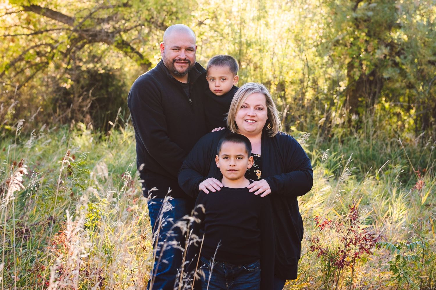 Family of four, posed family portrait, fall colors, sunbeam coming through trees.