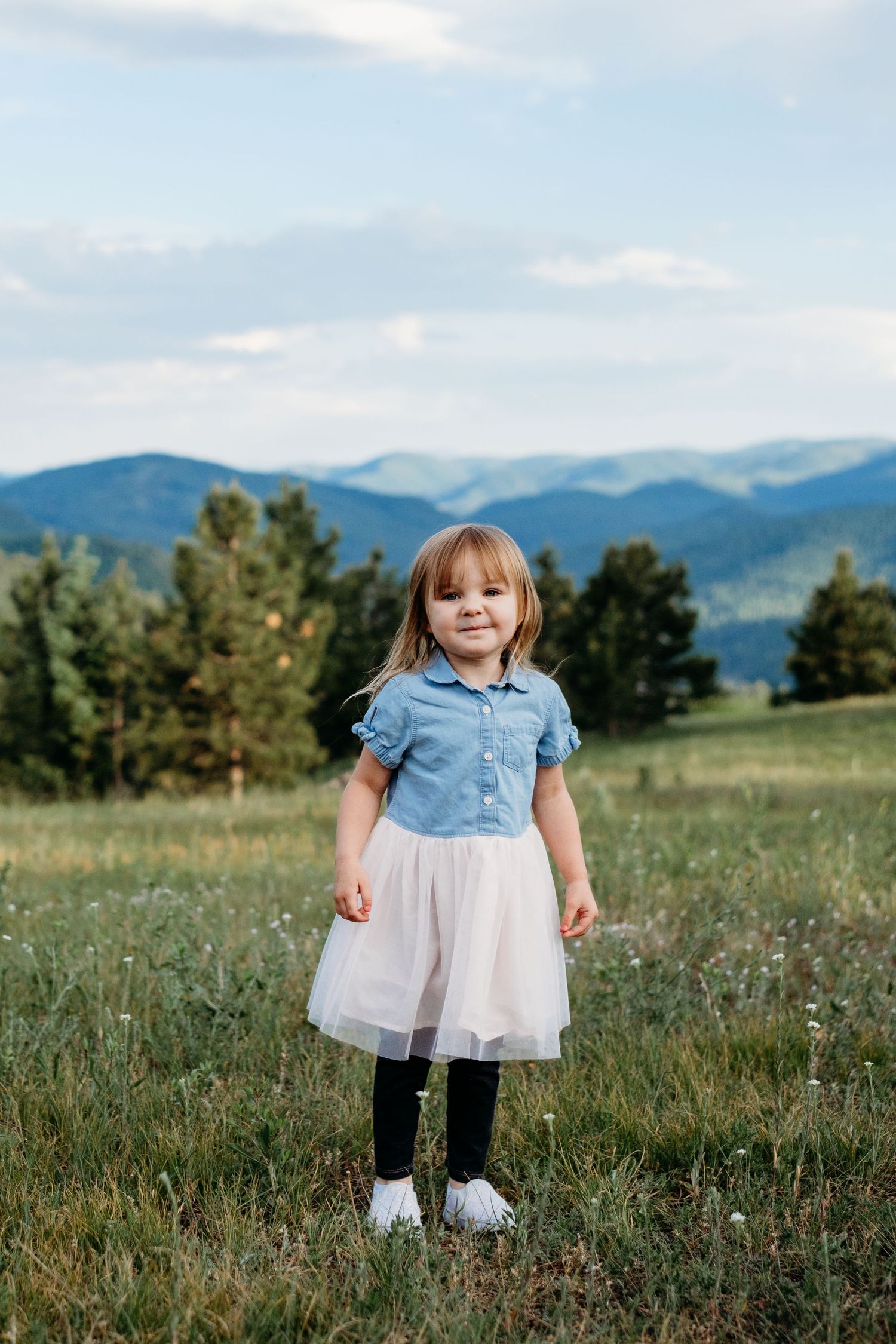 Young girl standing in Mount Falcon West meadow, evergreens and mountain views in background.