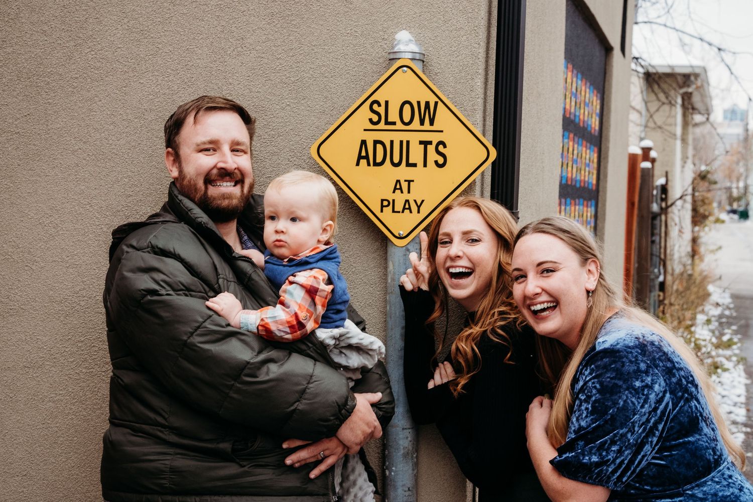 Three adult siblings and one toddler standing close together near sign that reads,