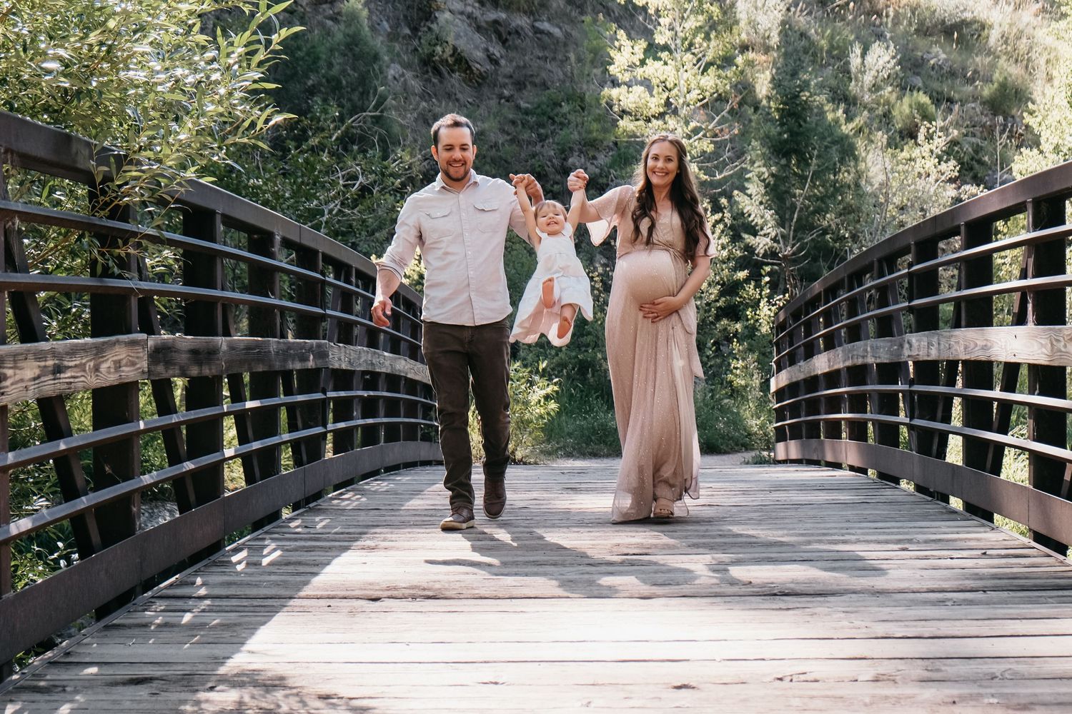 Father and pregnant mother on bridge in Lair O' The Bear, swinging toddler daughter into the air between them.