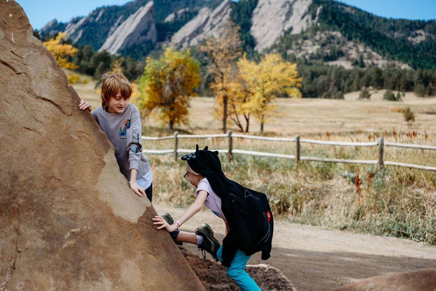 Boy and girl climbing on rock structure with Boulder flatirons in the background.