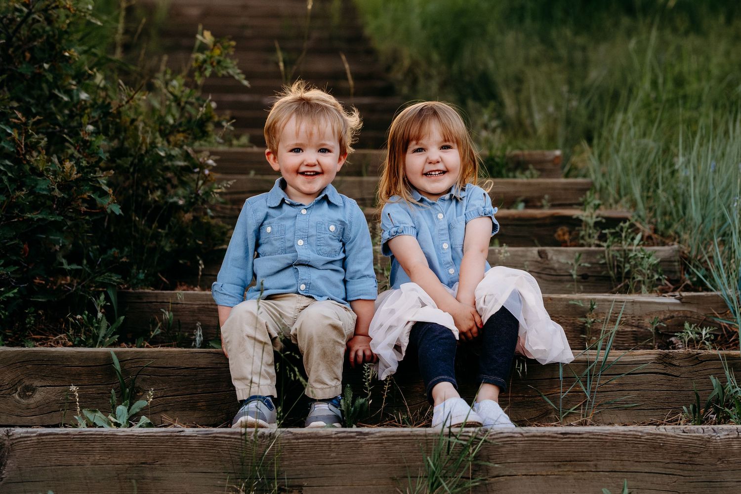Close up of toddlers sitting on wooden steps, both smiling widely.