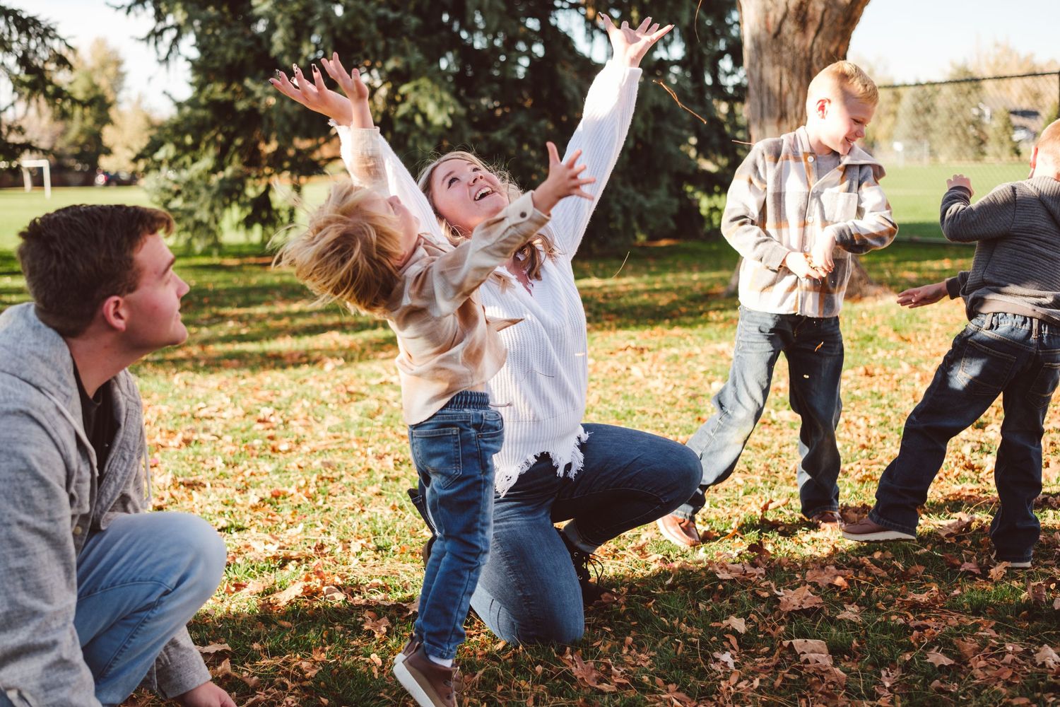 Cousins gleefully throwing leaves in the air in park in Denver metro area.
