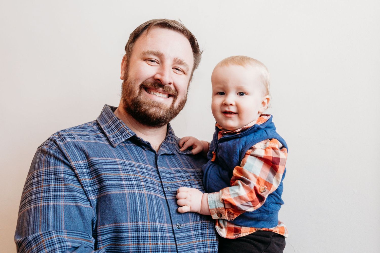 Studio portrait of father holding toddler son, both smiling.