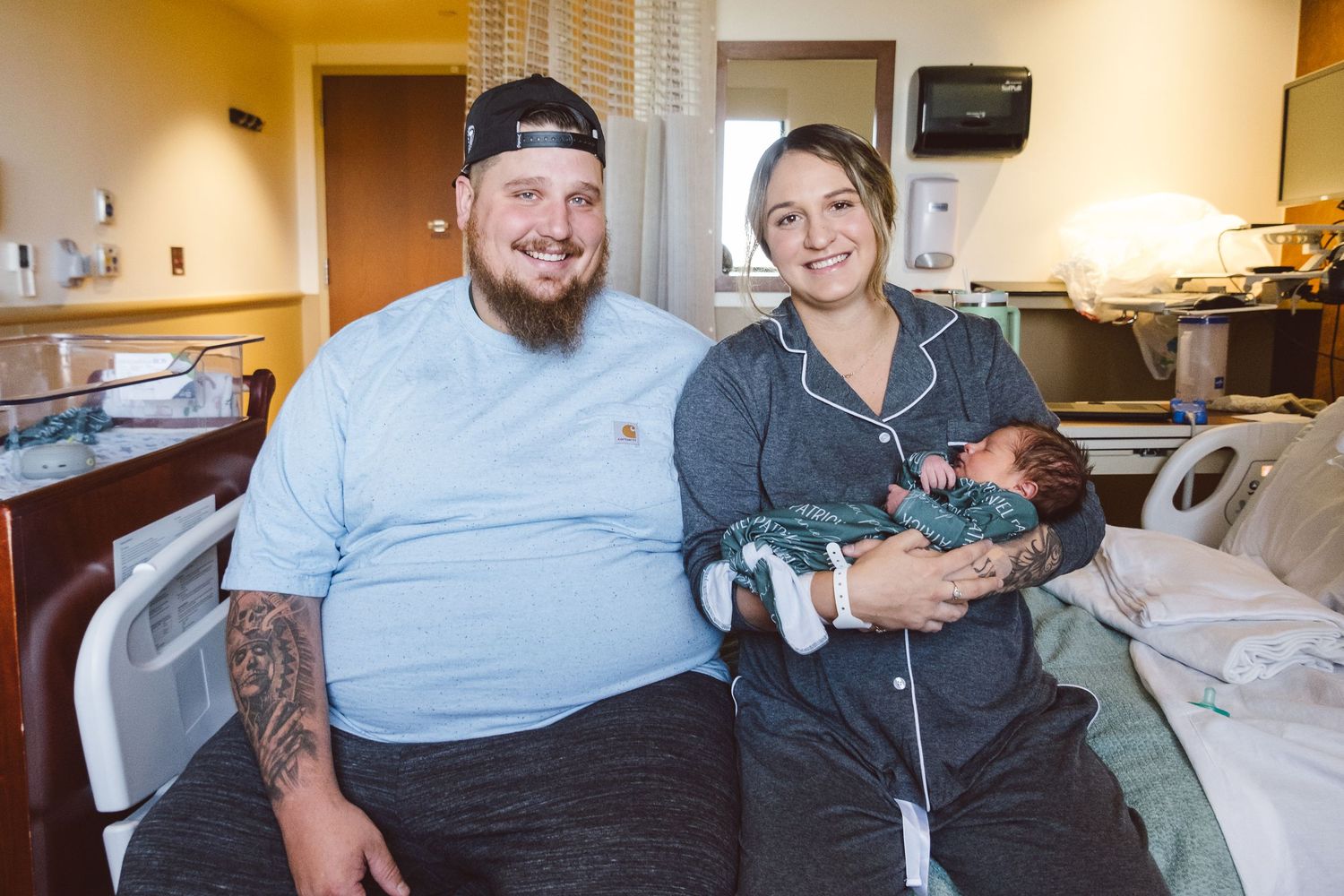Mother and father holding baby while sitting on hospital bed in their hospital room in Fresh 48 session in Littleton, Colorado.