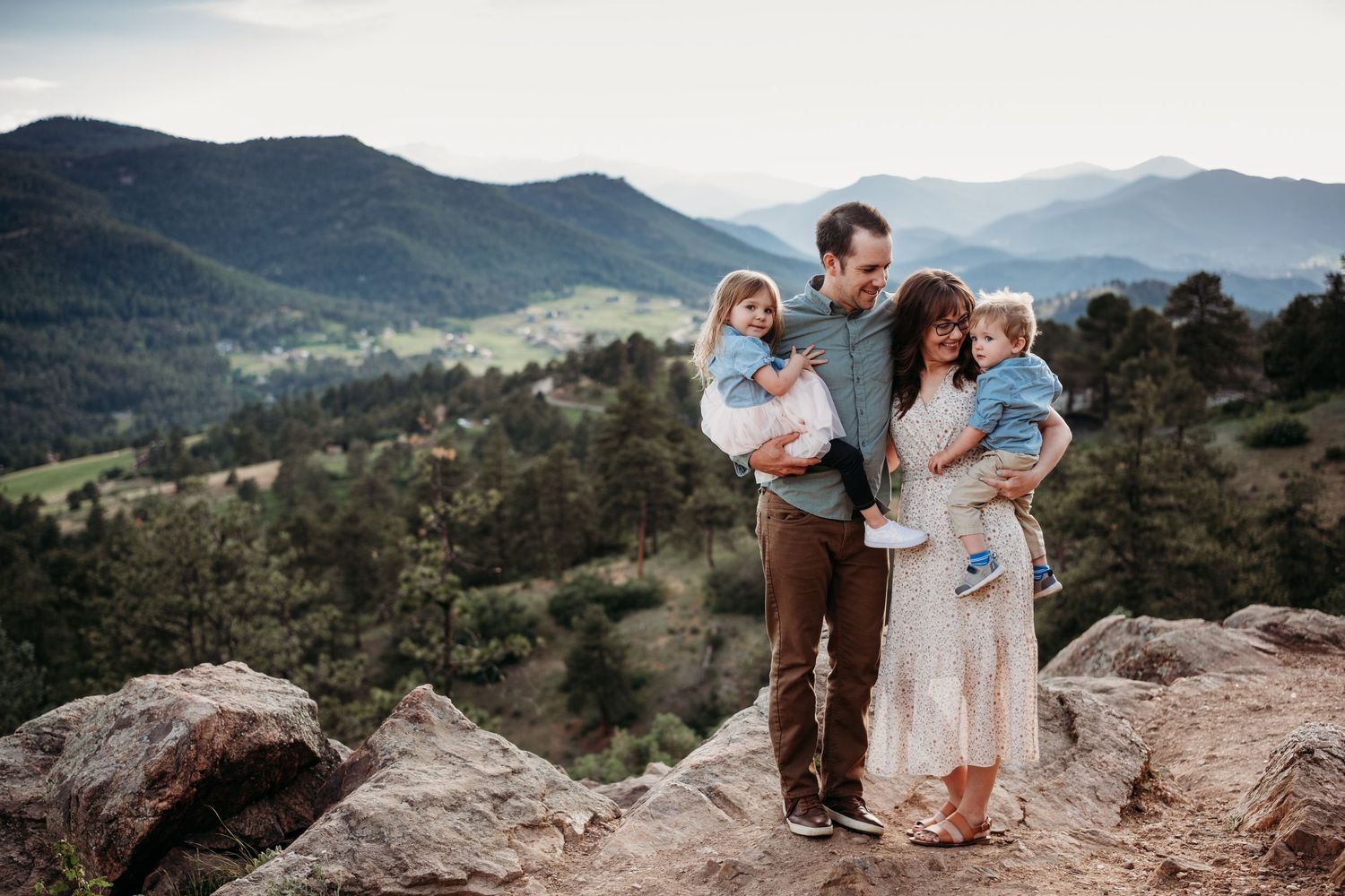 Family of four standing on rocks at Mount Falcon West, stunning views of evergreen filled mountains in background.