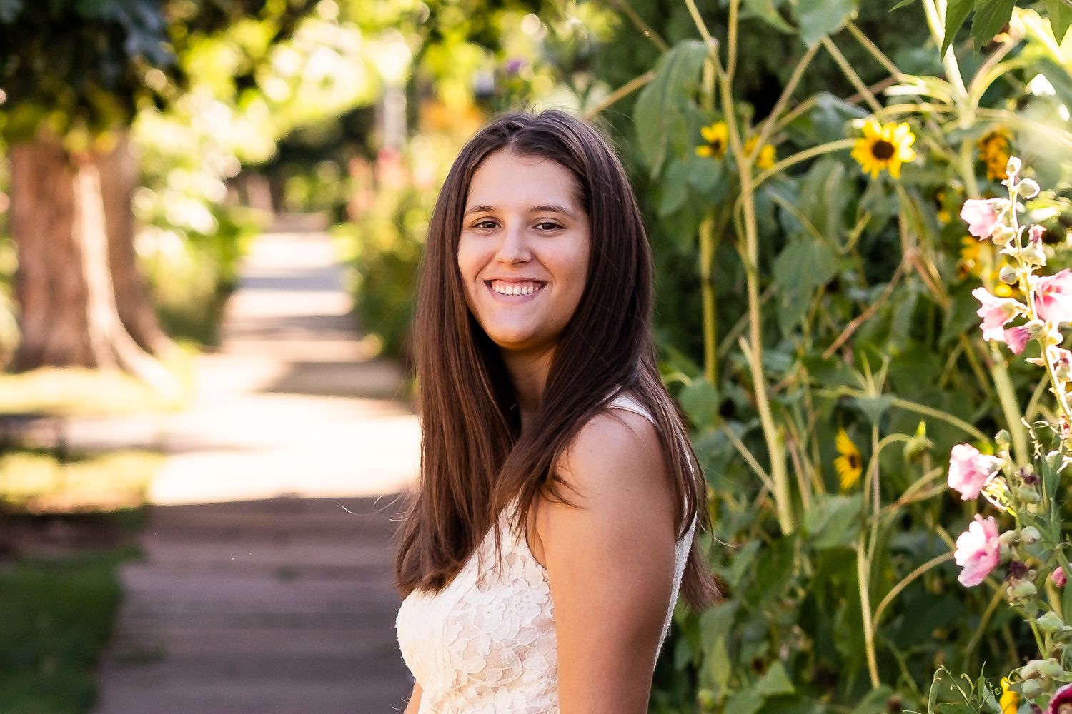 Teen girl smiling by tall sunflowers in Golden neigbohrhood.