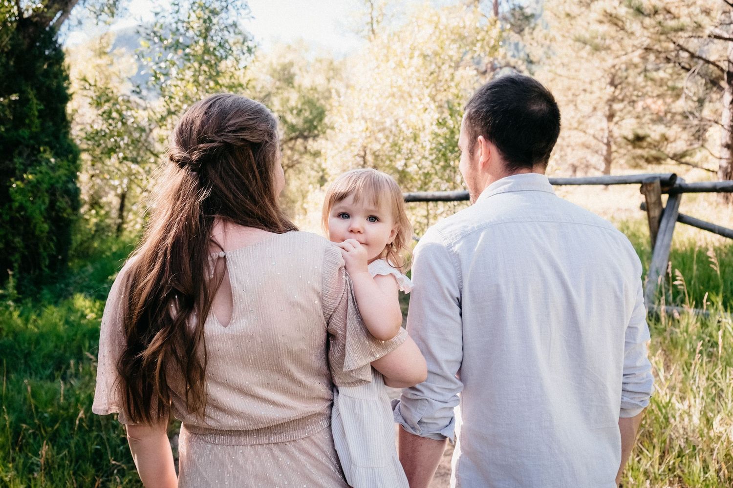 Mother and father walking away, mother holding toddler daughter on her hip, toddler peaking over mother's shoulder.
