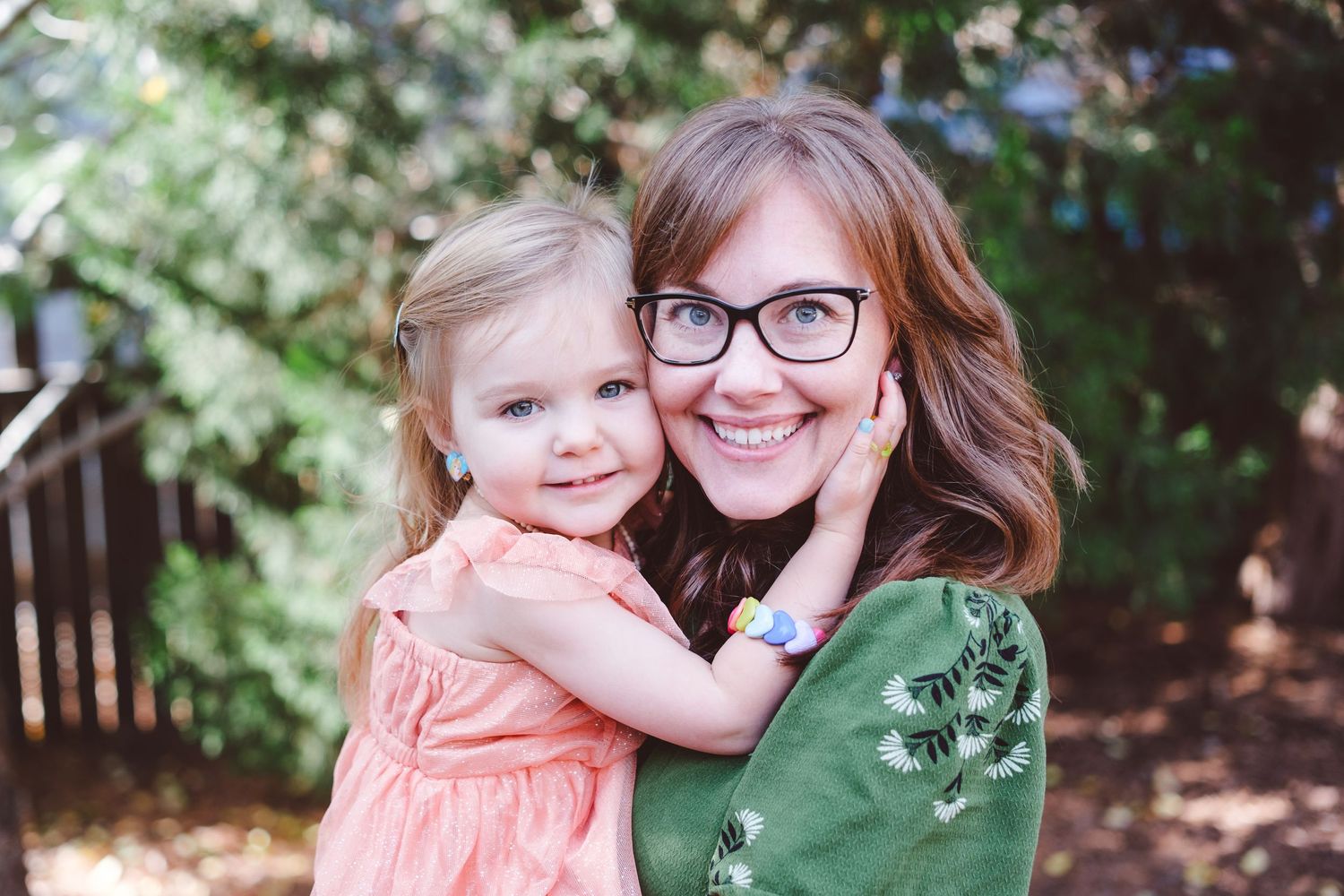 Mother in green dress snuggling daughter, cheek to cheek.