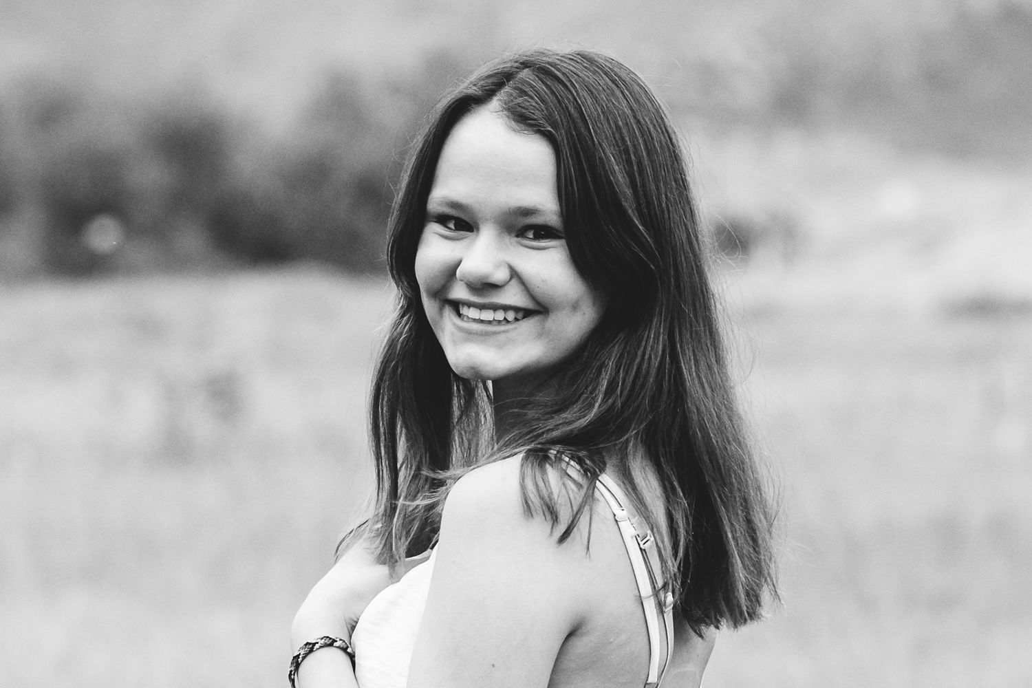 Black and white close up of teen girl peering over her shoulder, smiling.