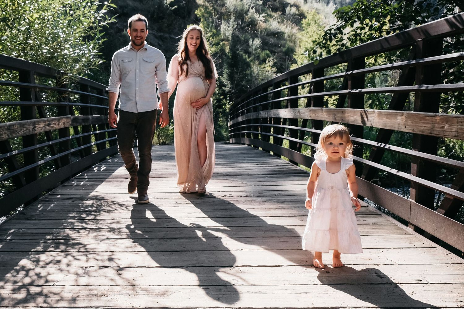 Toddler walking in front of father and pregnant mother on bridge in Lair O' The Bear.