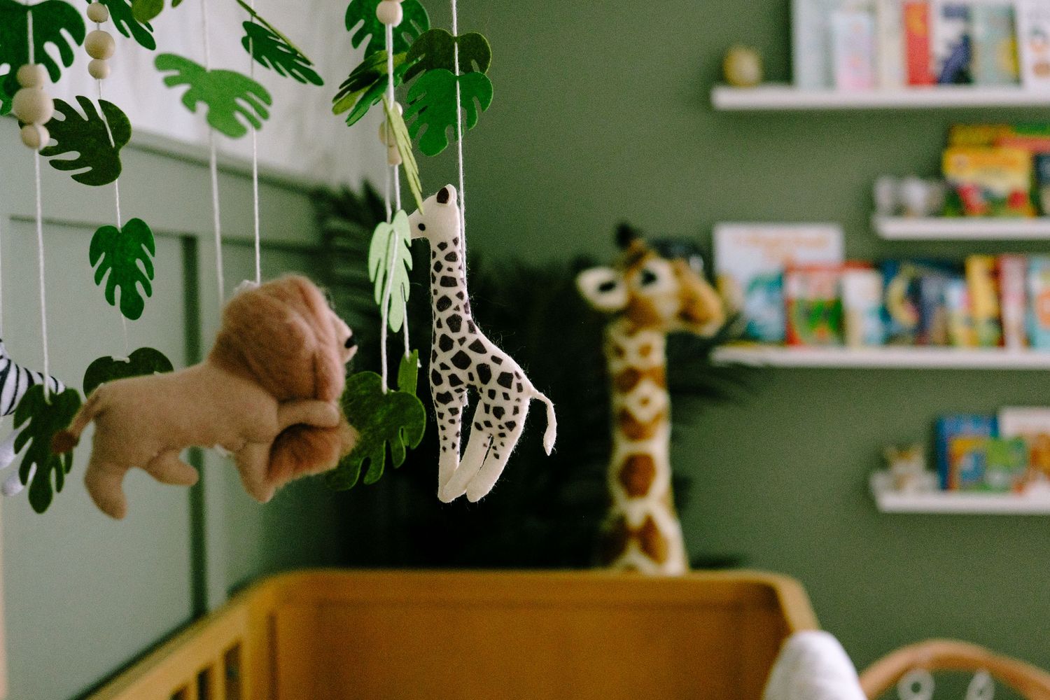 Close up of lion, giraffe and leaf mobile above baby crib in nursery.