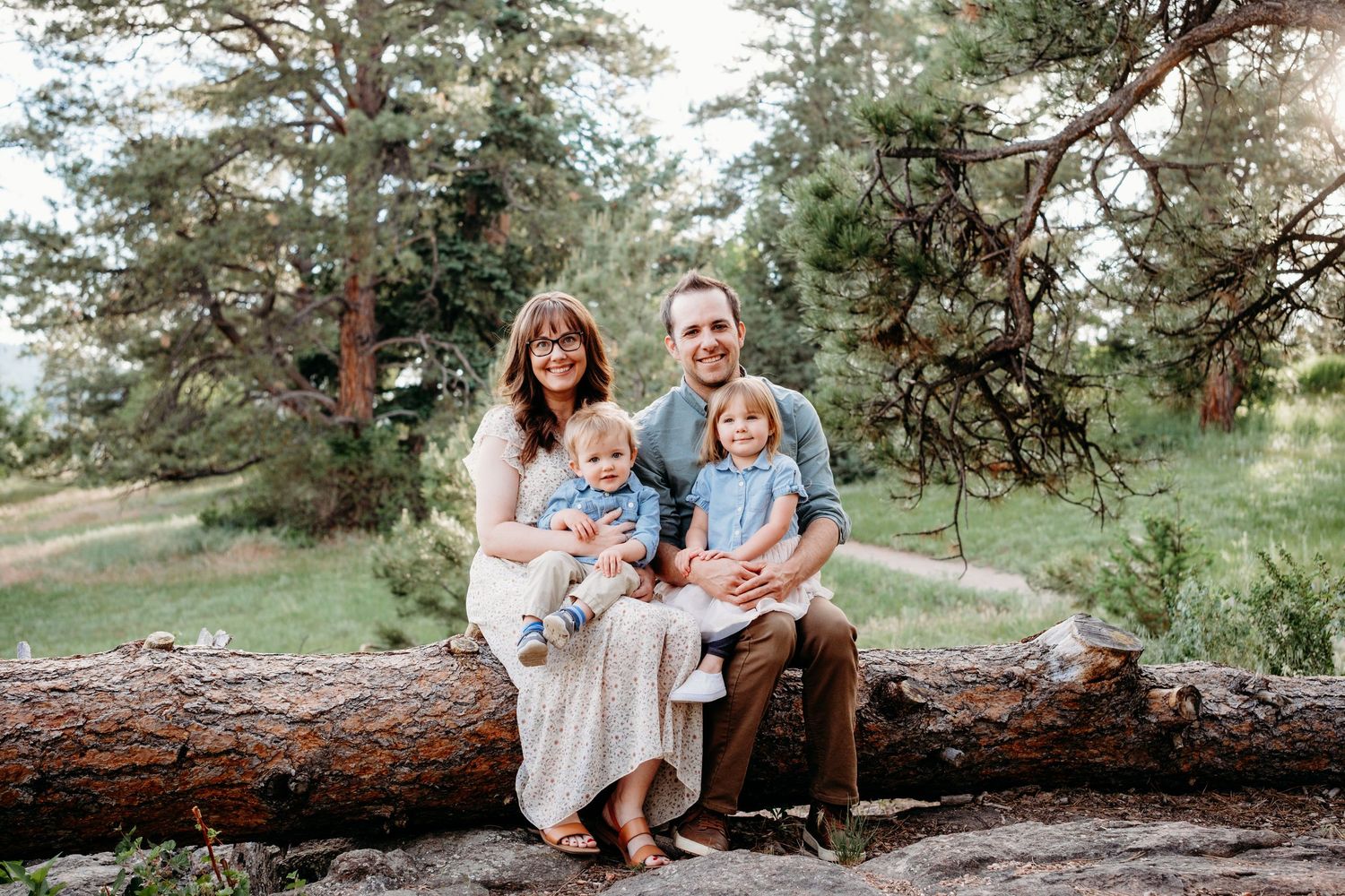 Father and mother sitting on fallen tree trunk, children sitting on their laps, all smiling.
