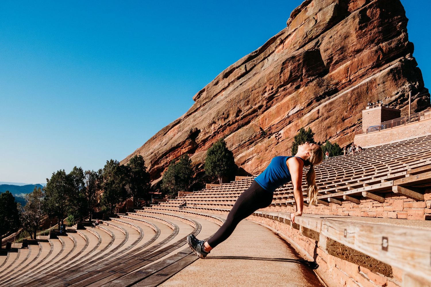Fitness branding photography at Red Rocks in Denver Colorado, female trainer doing stretch on steps of Red Rocks.