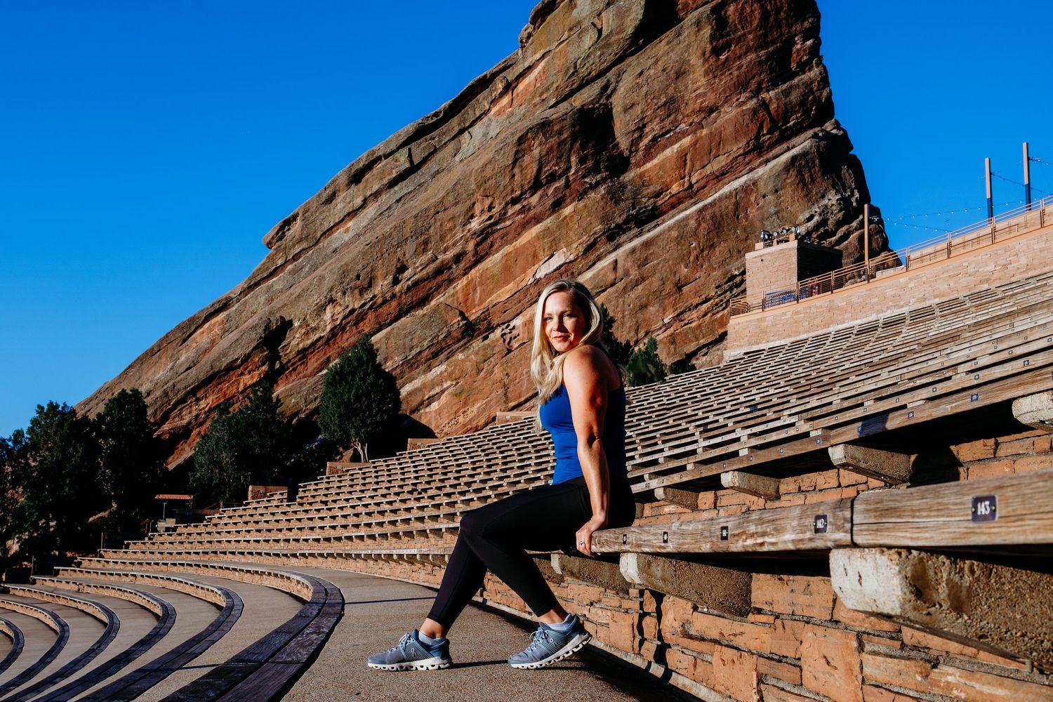 Fitness branding photography, Progress with Paige sitting on steps of Red Rocks, Red Rock formation in background with vibrant blue skies.
