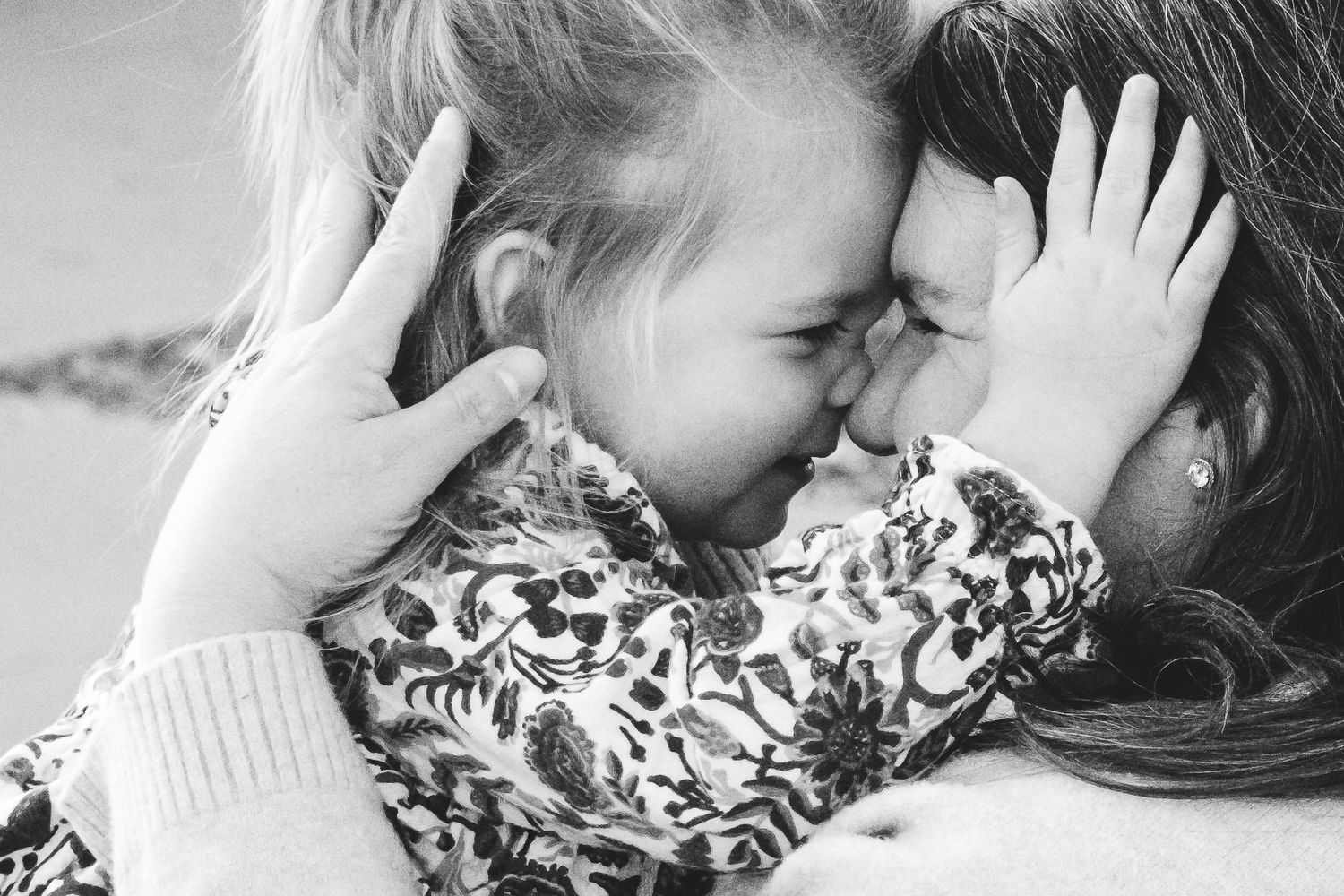 Close up of mother and toddler daughter squishing together, nose to nose, smiling.