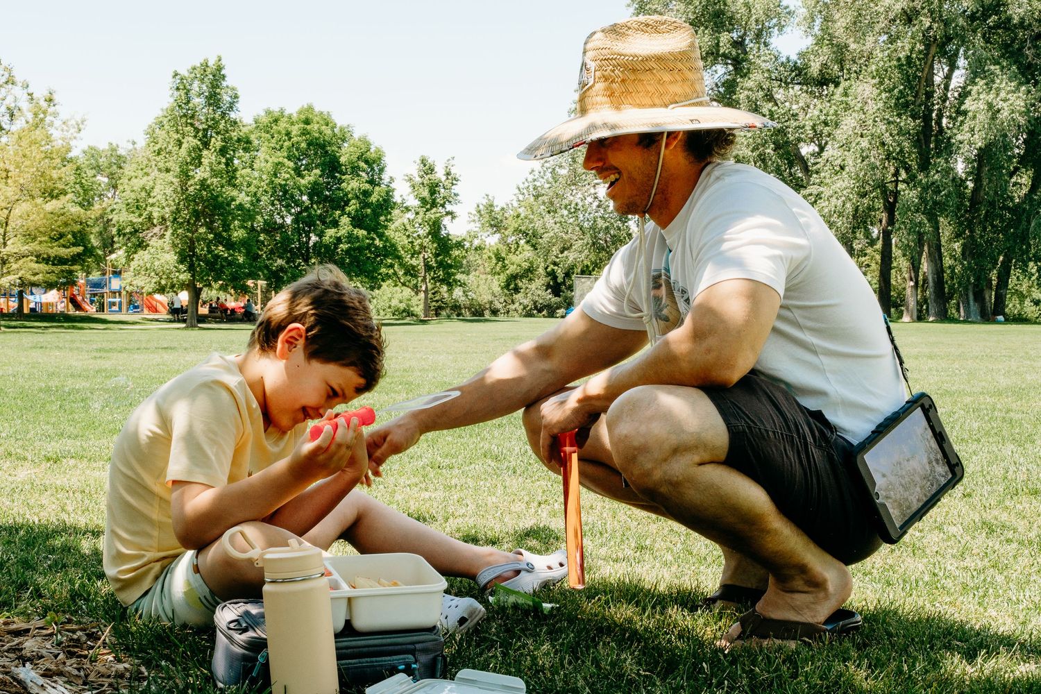 Father and son playing bubbles under the shade of a tree on a sunny day at Denver metro area park.