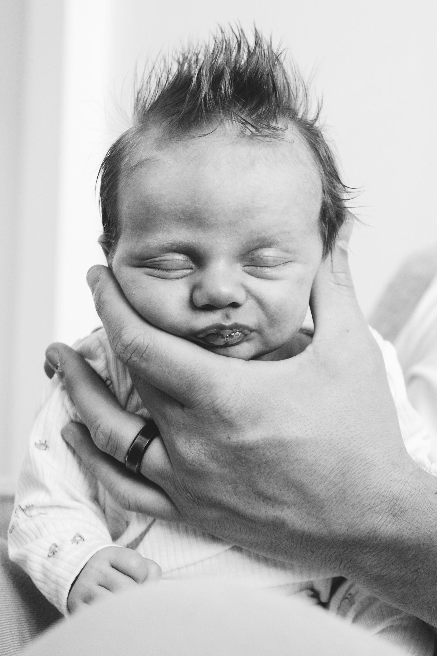 Black and white close up of newborn baby boy with spit bubbles near pouty lips during Denver in-home photo session