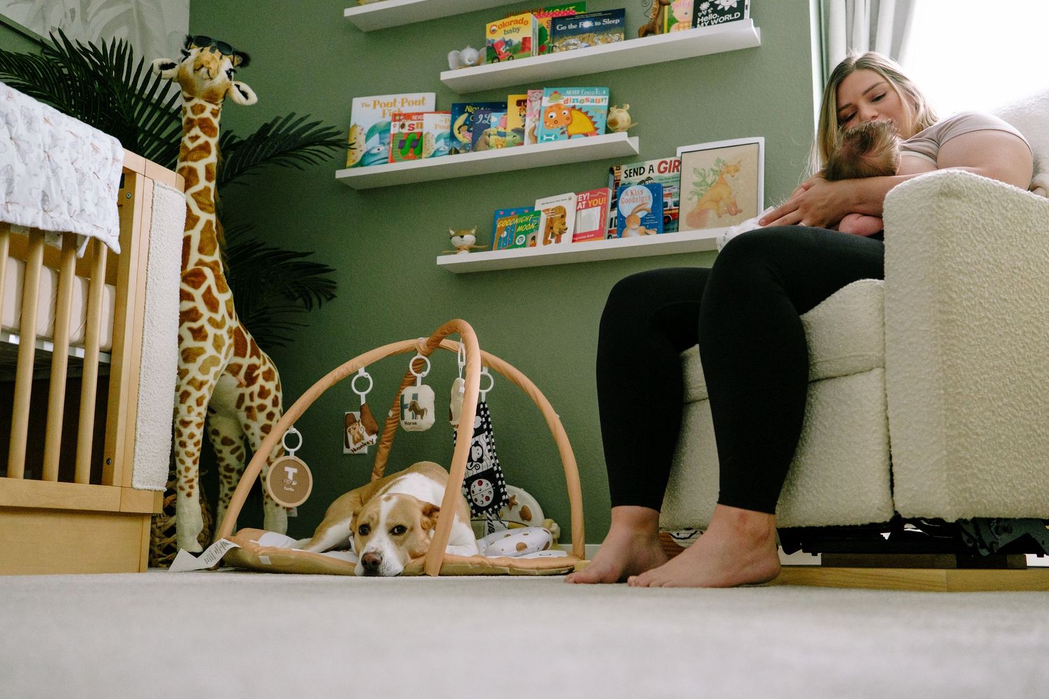 Mother feeding baby on rocker, dog sitting on newborn's activity mat in newborn nursery during Denver in-home photo session.