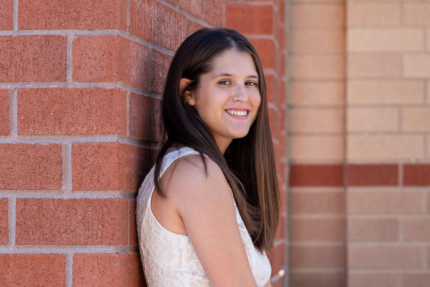 Senior portrait of teen girl leaning against brick wall.