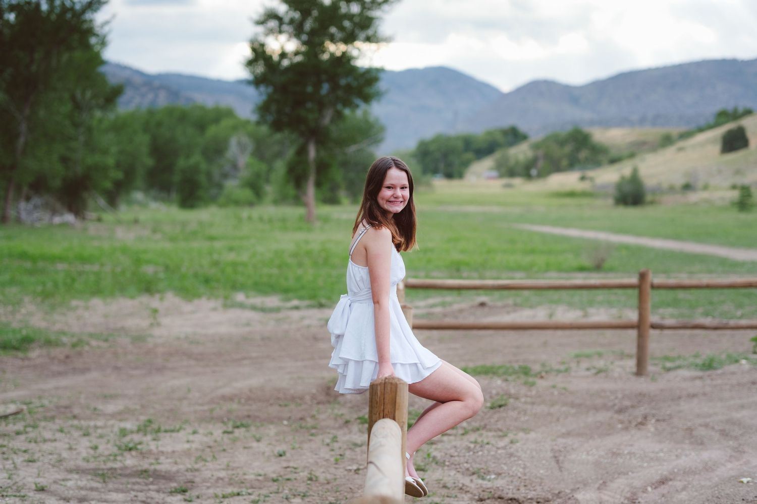 Teen girl sitting on wooden fence rail at Bear Creek Lake in Lakewood, Colorado.