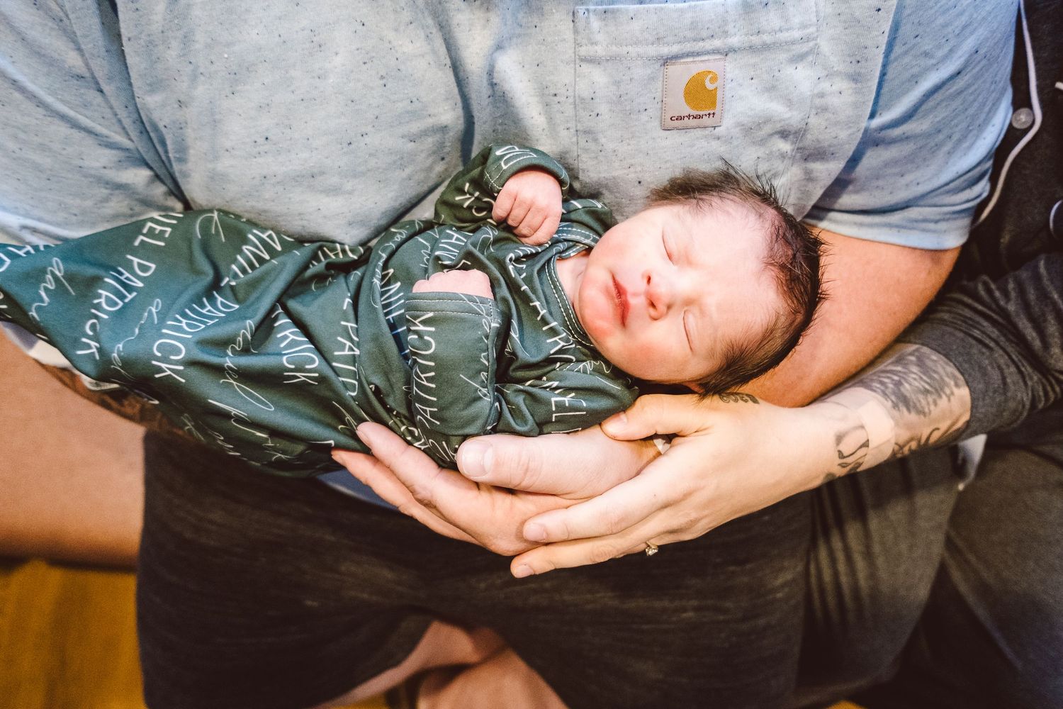 Newborn baby being held in father's arm, mother holding father's hand gently, newborn baby sleeping.