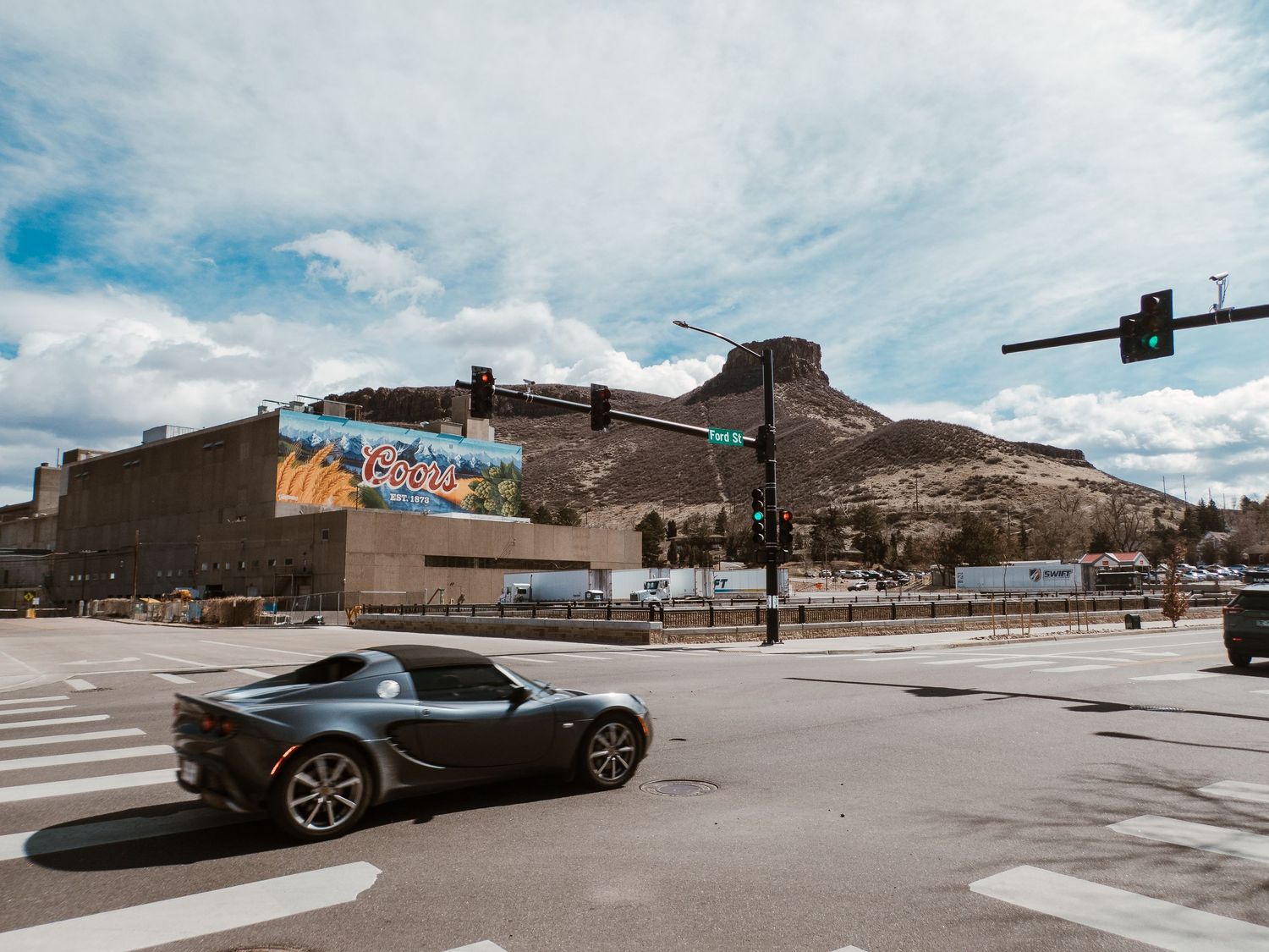 Sports car driving on street, Coors brewery in background in Golden CO.