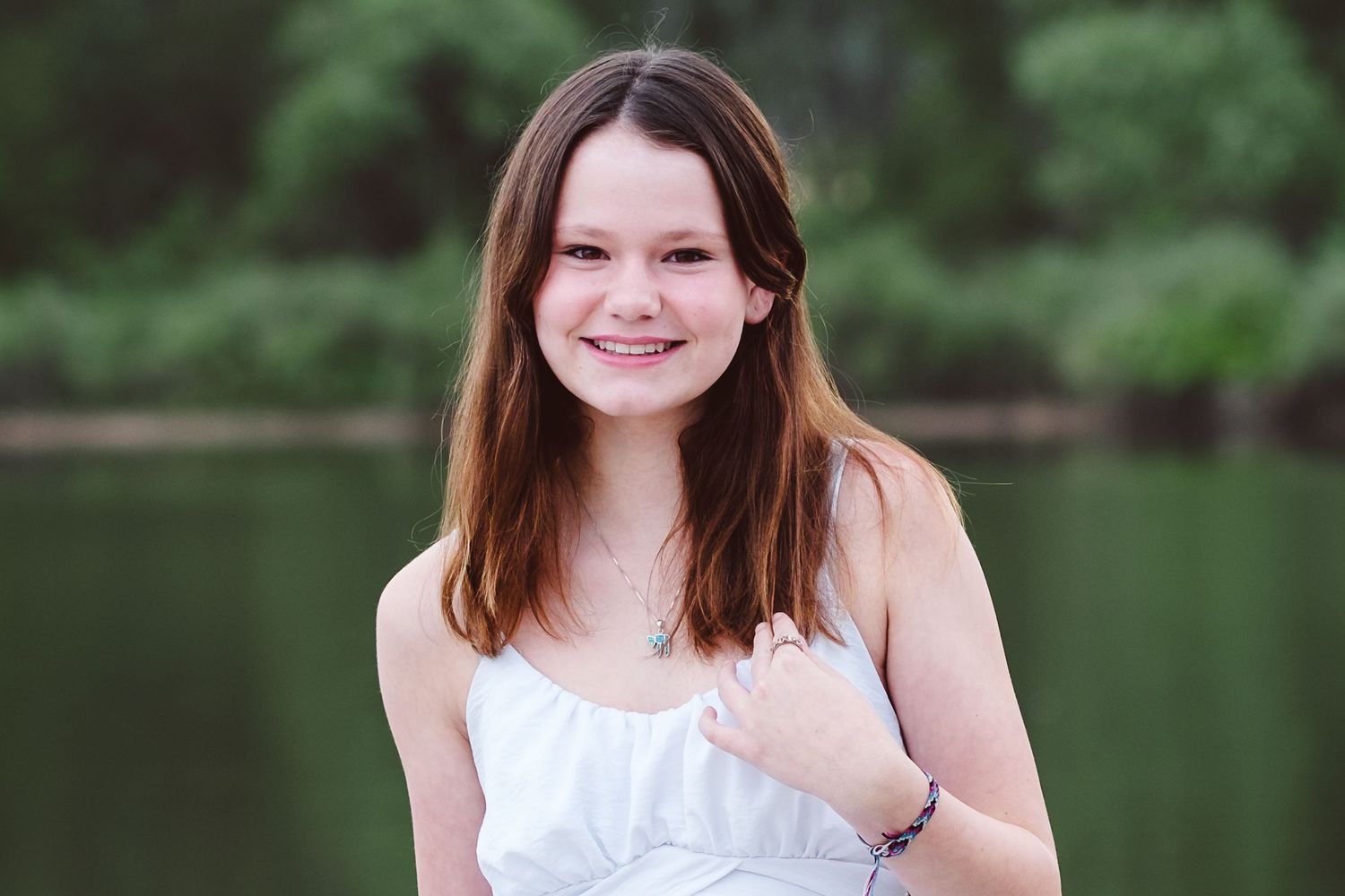Teen girl standing in front of water and green trees.