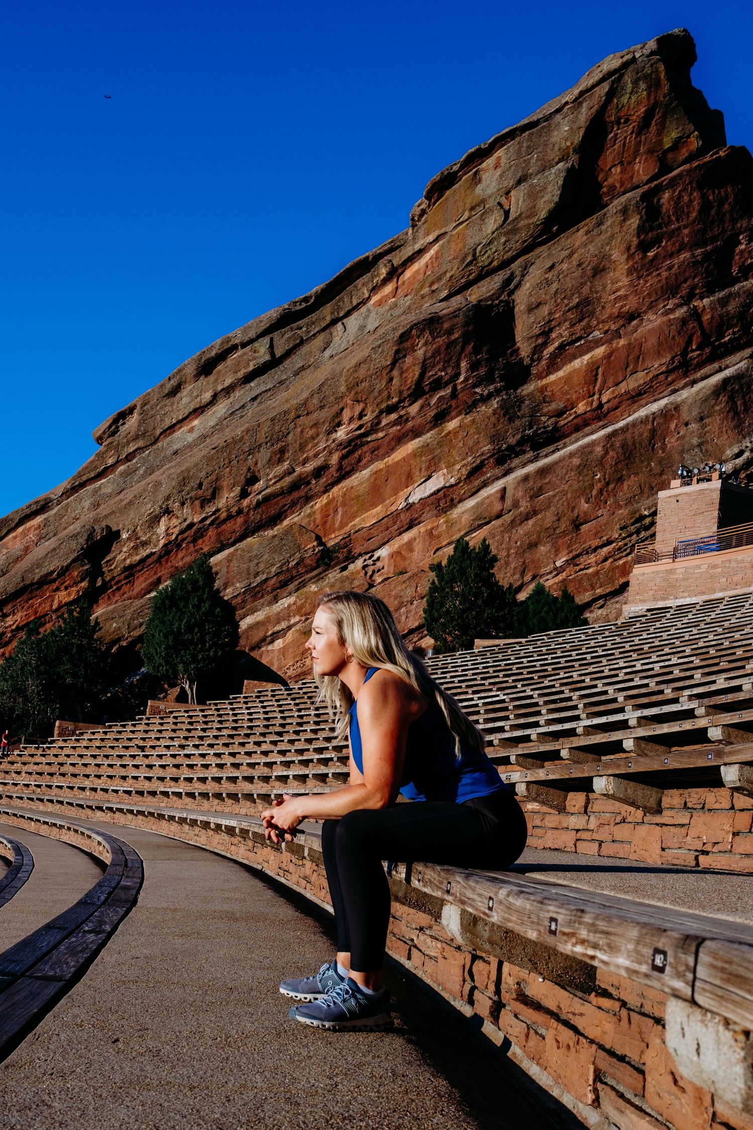 Dramatic portrait of female trainer sitting at Red Rocks Amphitheater, Red Rocks formation behind her with vibrant blue skies.