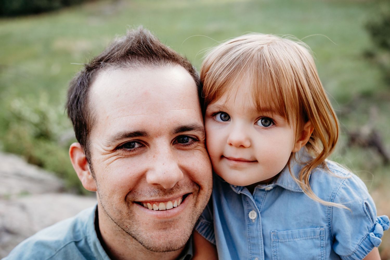 Close up of father and young daughter snuggling cheek to cheek, both smiling.