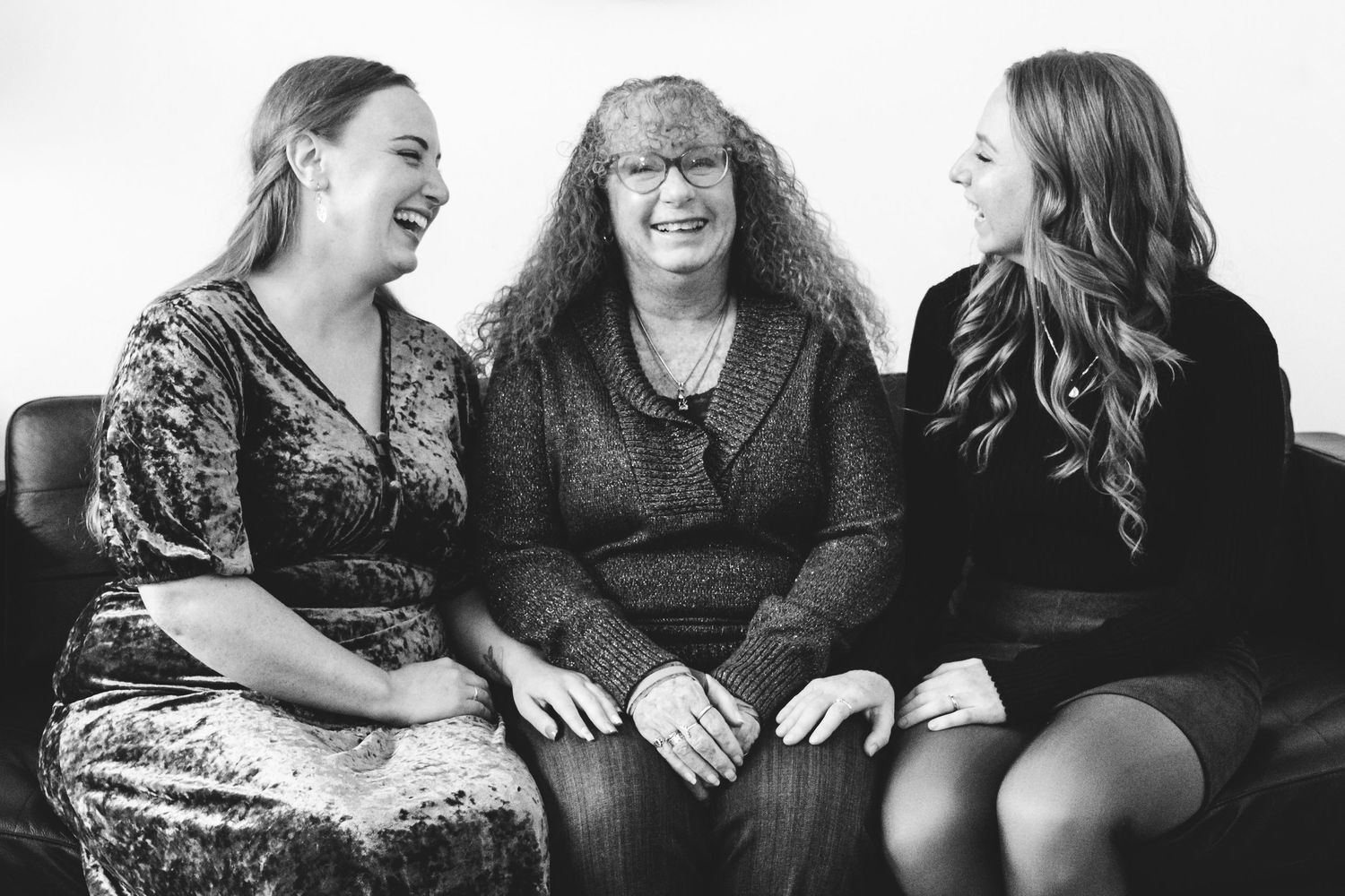 Black and white of mother and two adult children, all looking at one another laughing.