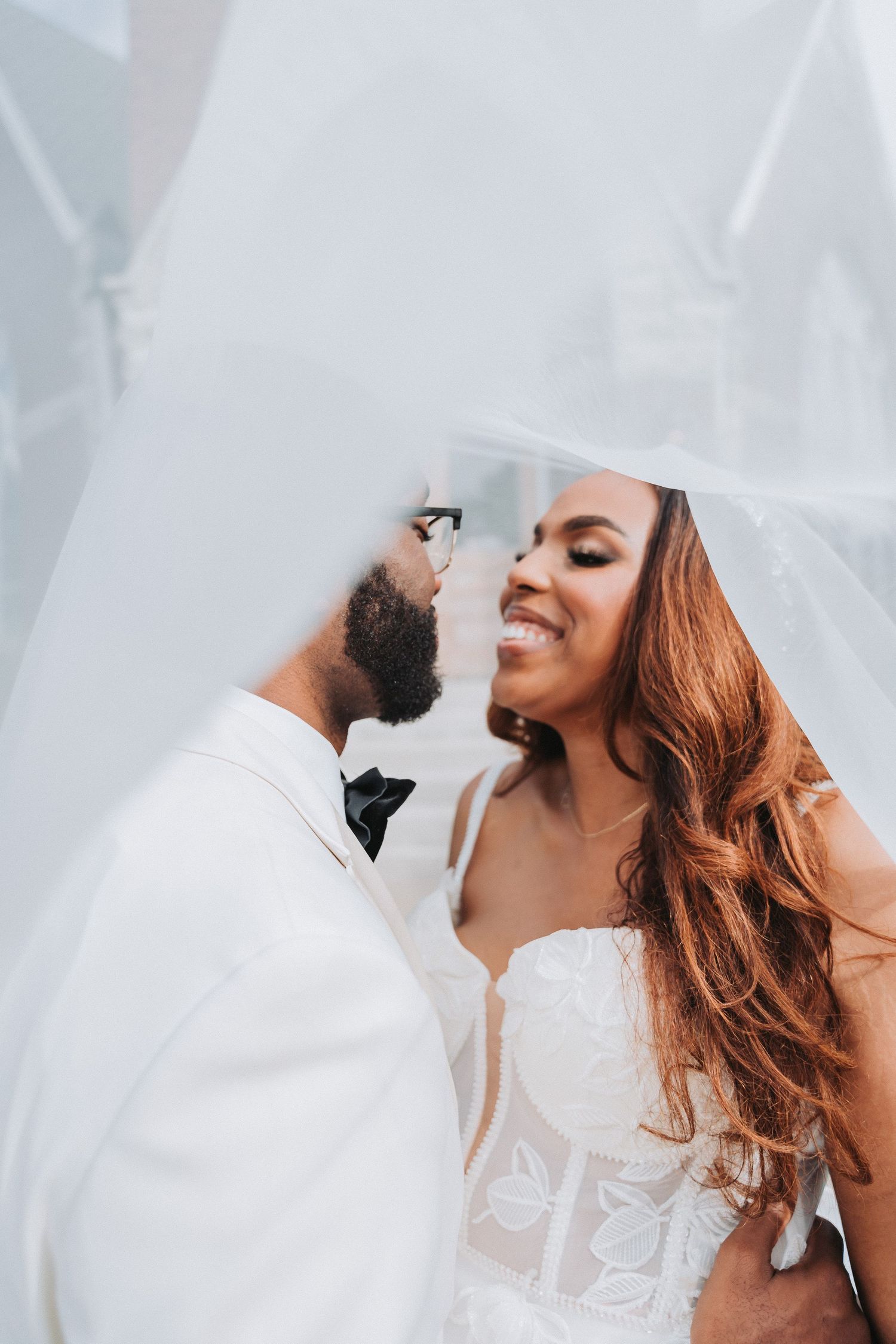 Romantic wedding portrait through delicate white veil in natural lighting.