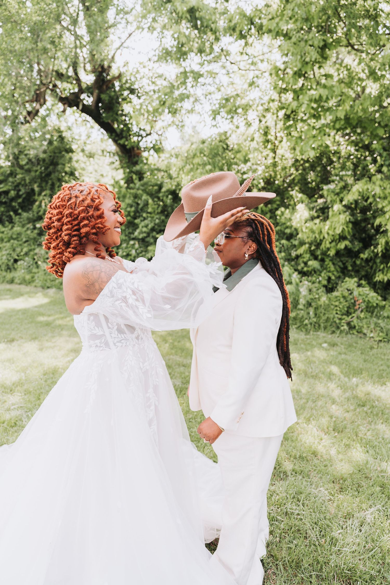Two people in white wedding attire dance and celebrate together in a lush green garden setting.