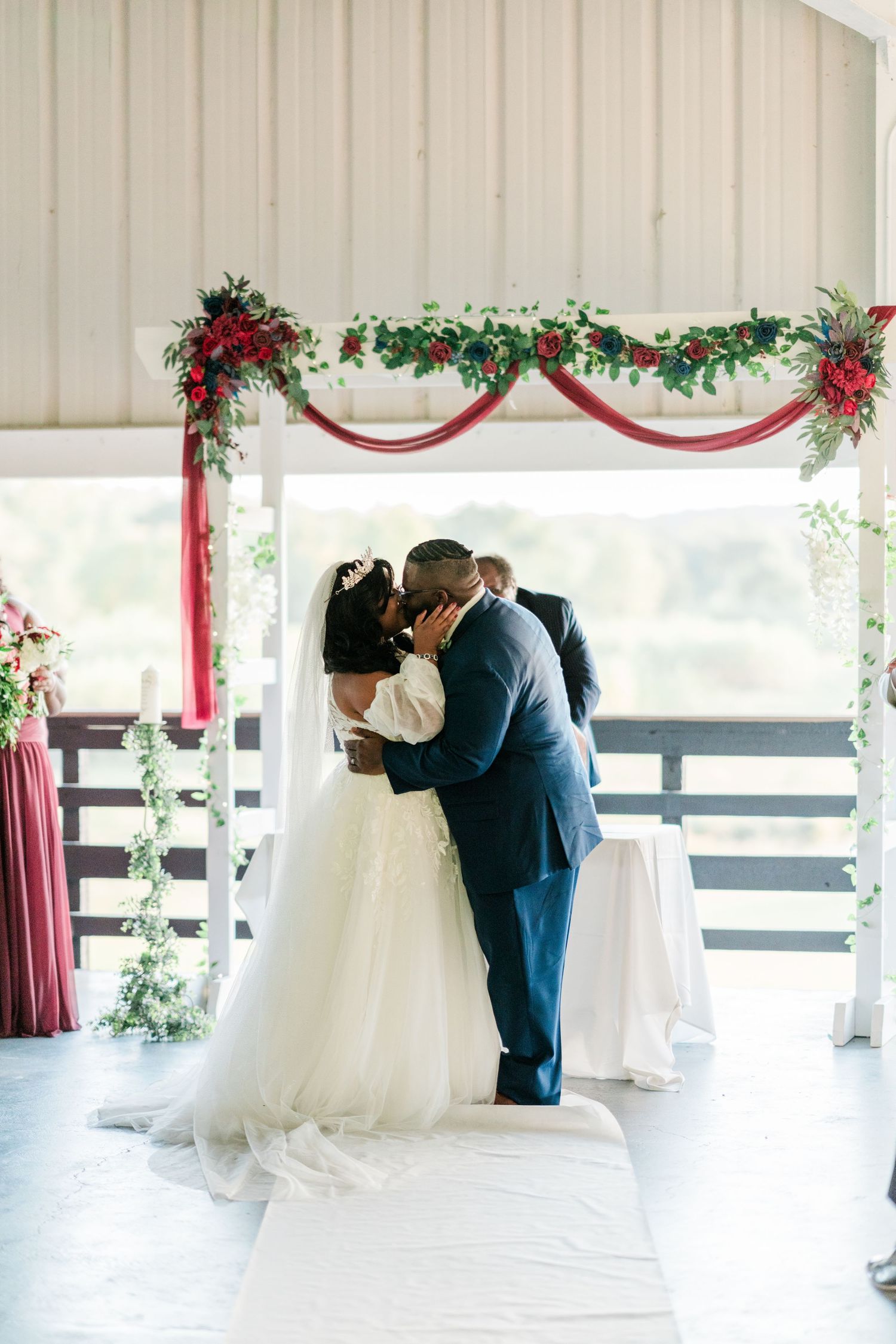 Wedding ceremony under an arch decorated with burgundy fabric and floral arrangements.