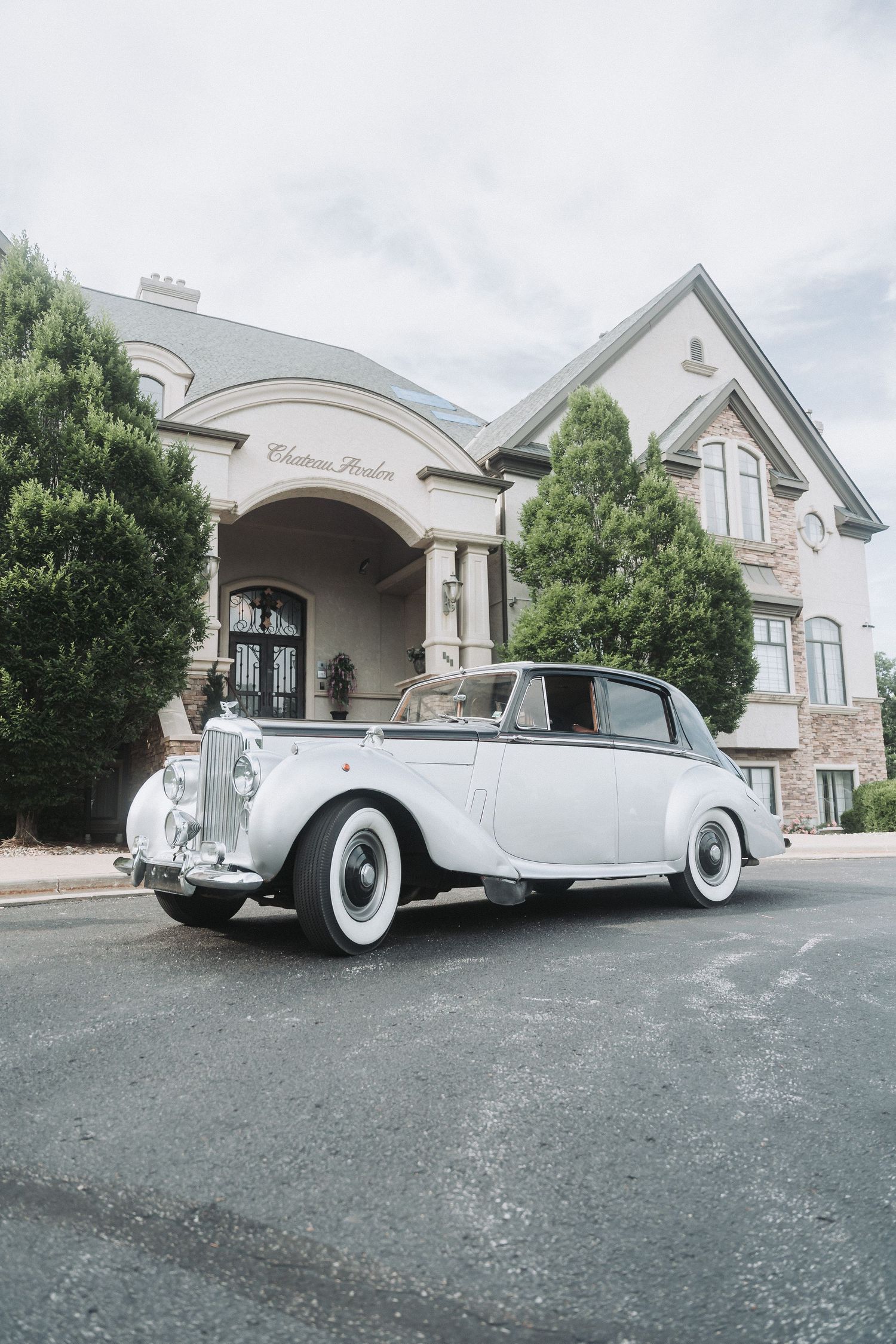 Classic white Rolls Royce parked in front of elegant mansion building.