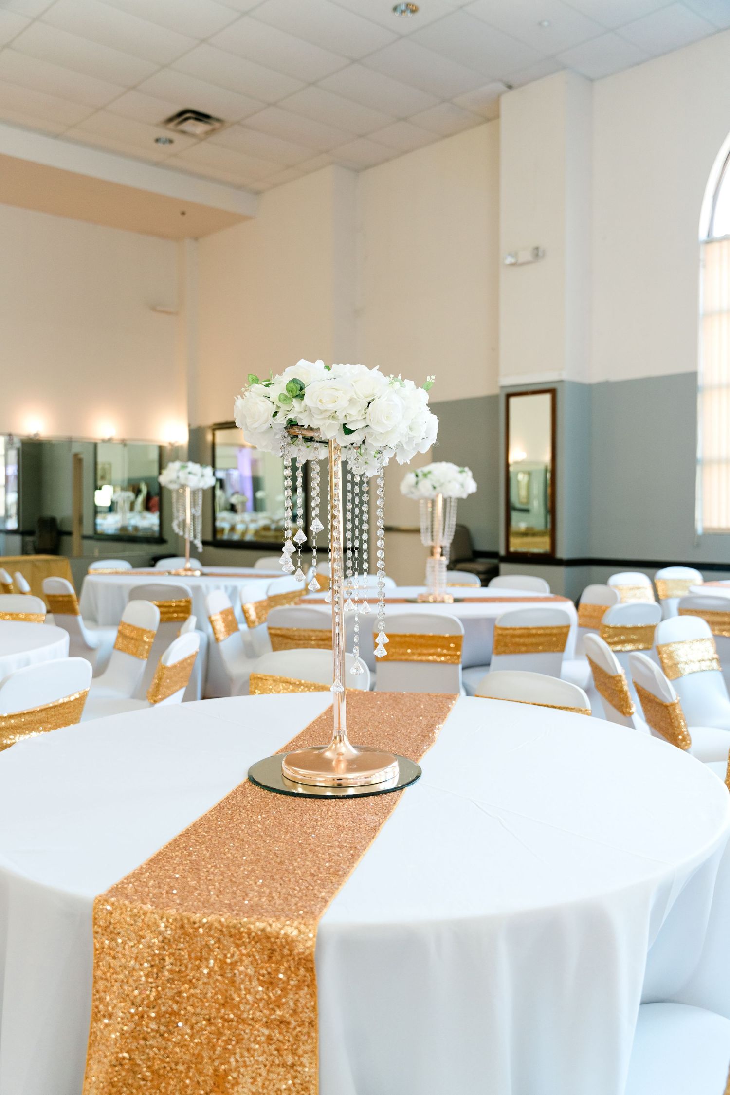 Elegant wedding reception table with white linens, gold sequin runners and crystal centerpiece with white orchids.