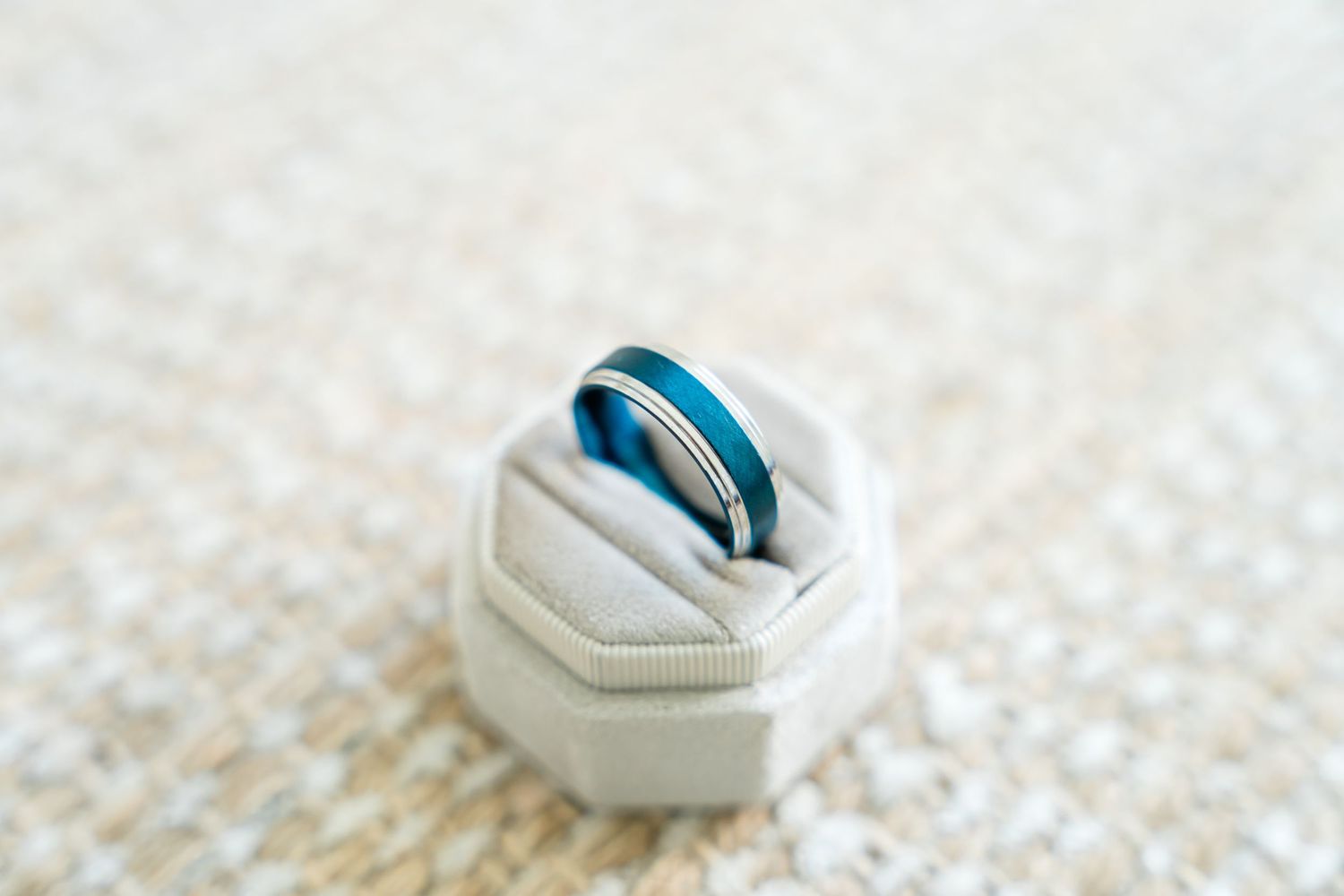 Blue wedding band resting on a white ring box against a textured cream background.