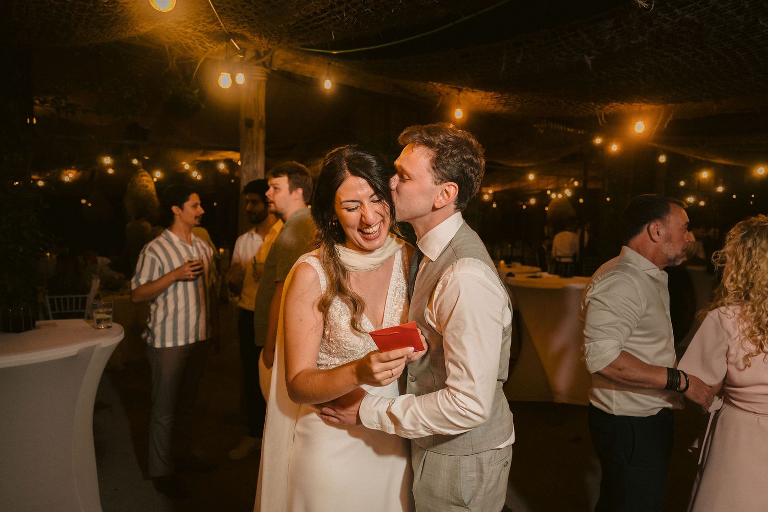 A modern wedding reception at night with dancing couples on the dance floor illuminated by warm overhead lights.