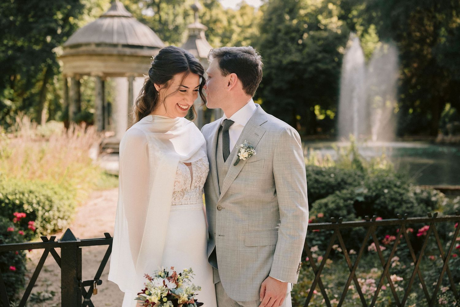 A romantic wedding moment captured in a garden setting with a gazebo, vintage bicycle, and soft sunlit background.
