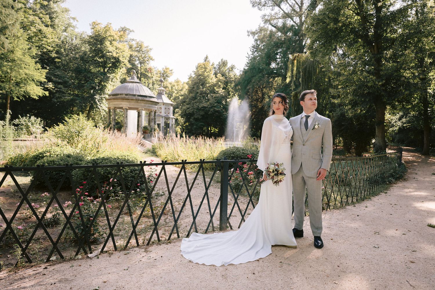Wedding moment captured on rustic garden path lined with wooden fencing and lush greenery.