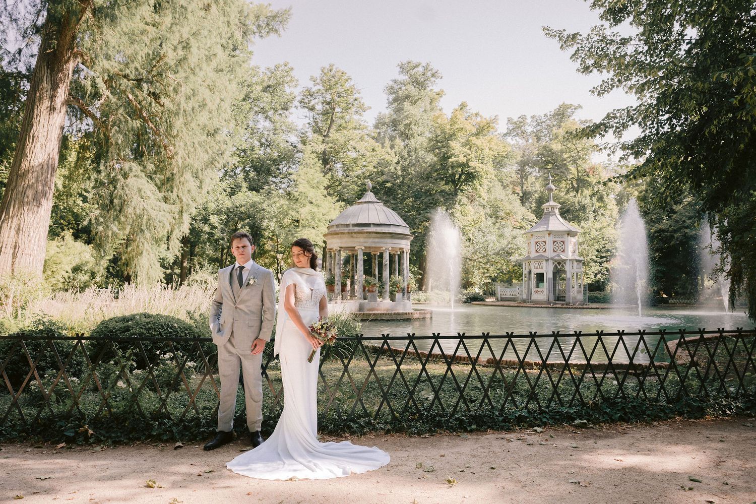 Elegant wedding photography in serene garden setting with decorative lattice fencing and gazebo.