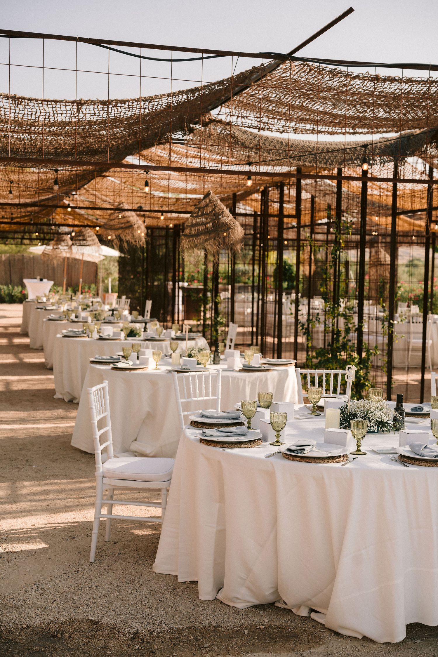 Rustic outdoor wedding reception setup with white tables and natural shade coverings creating a romantic atmosphere.