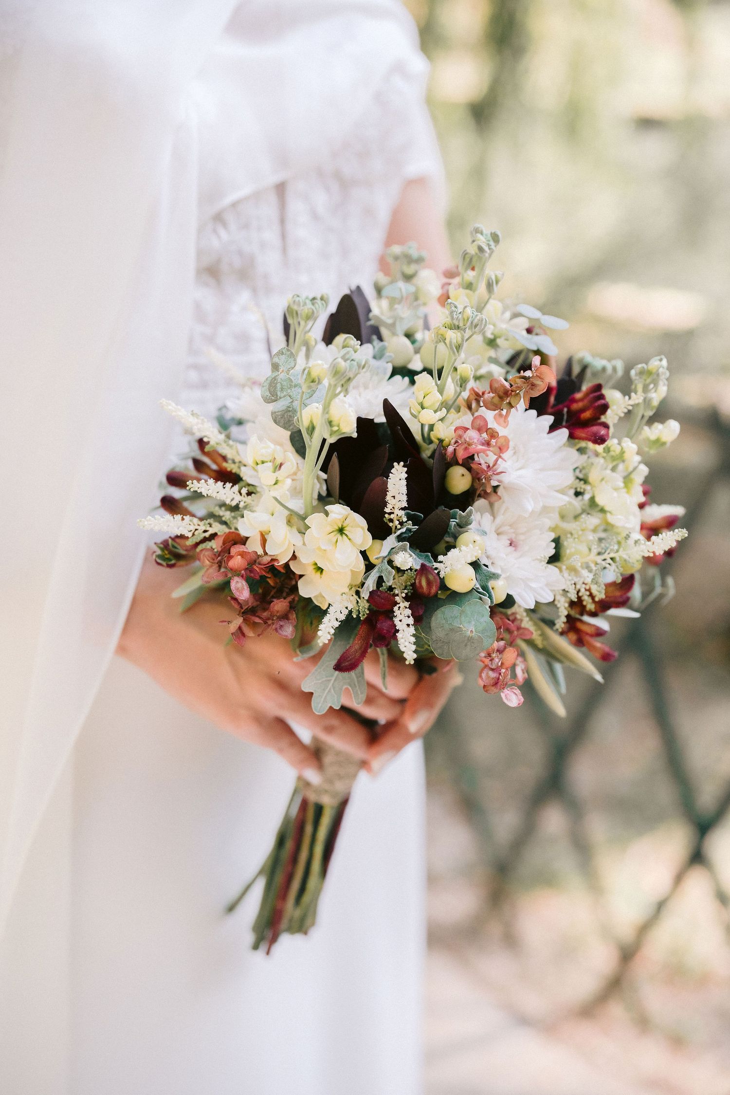 Close-up views of a delicate bridal bouquet featuring white, peach and burgundy flowers with eucalyptus greenery.