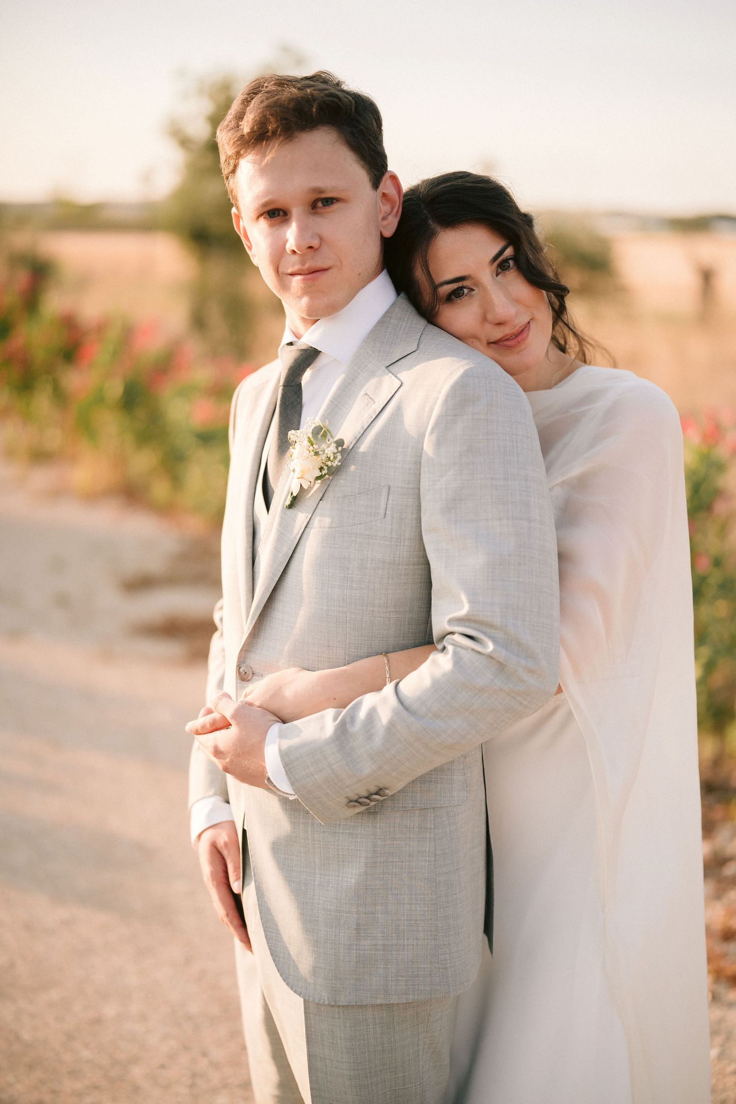 Wedding couple embracing in warm sunset light against a natural outdoor backdrop.